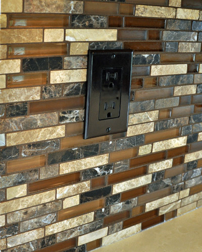 A stone and glass mosaic backsplash is perfect compliment to the Caesarstone counter and tile floors.  The dark outlet trim minimizes its impact visually. The paint colors selected by the clients compliment all of these beautifully--a pleasing and warm combination of colors